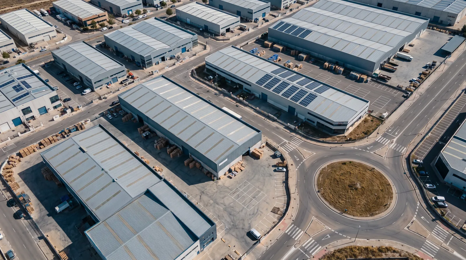 Polígono industrial visto desde el aire, con naves de cubierta gris, algunas con paneles solares, patios de carga y una rotonda.